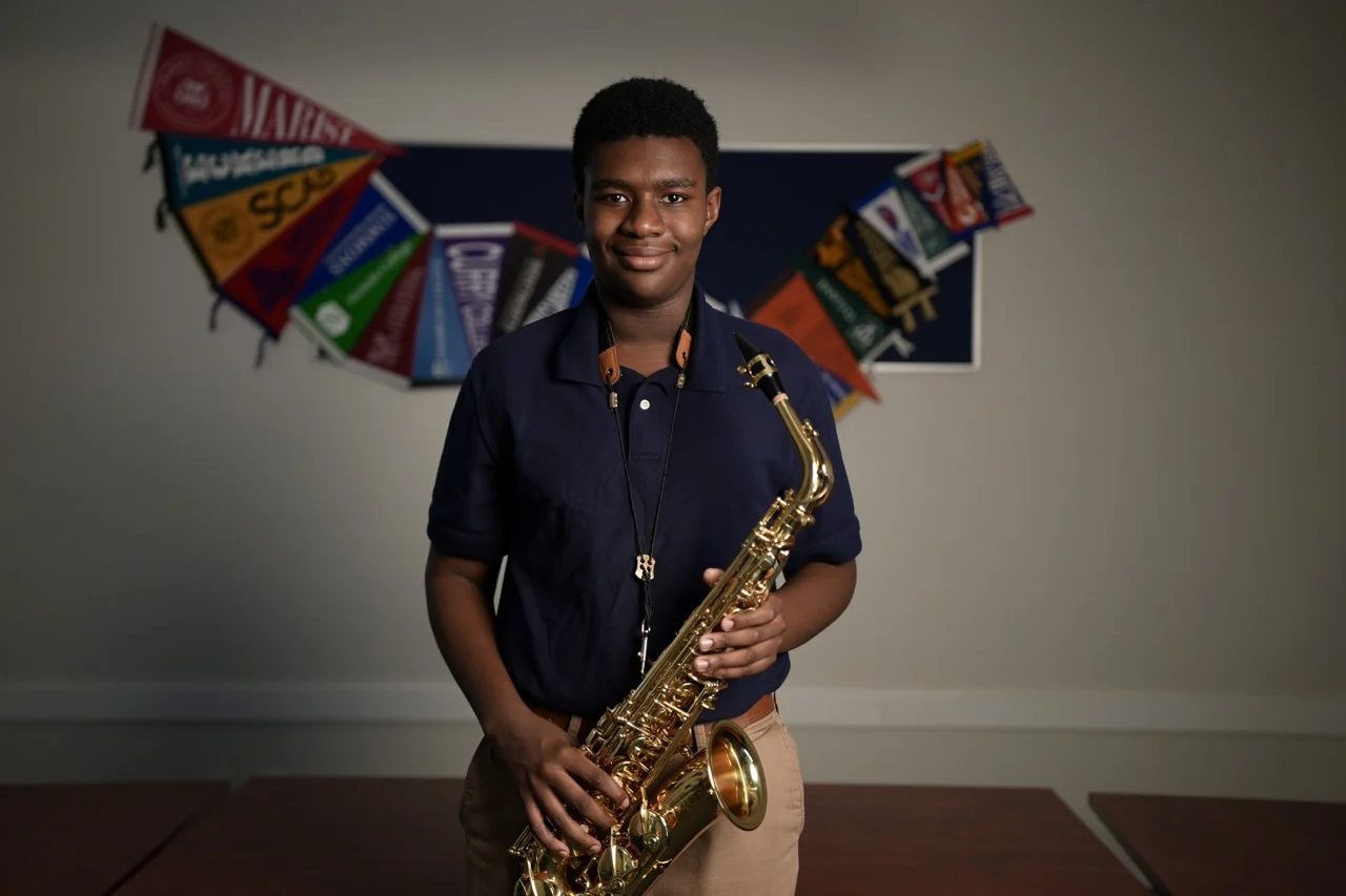 boy holding saxaphone with college banners behind